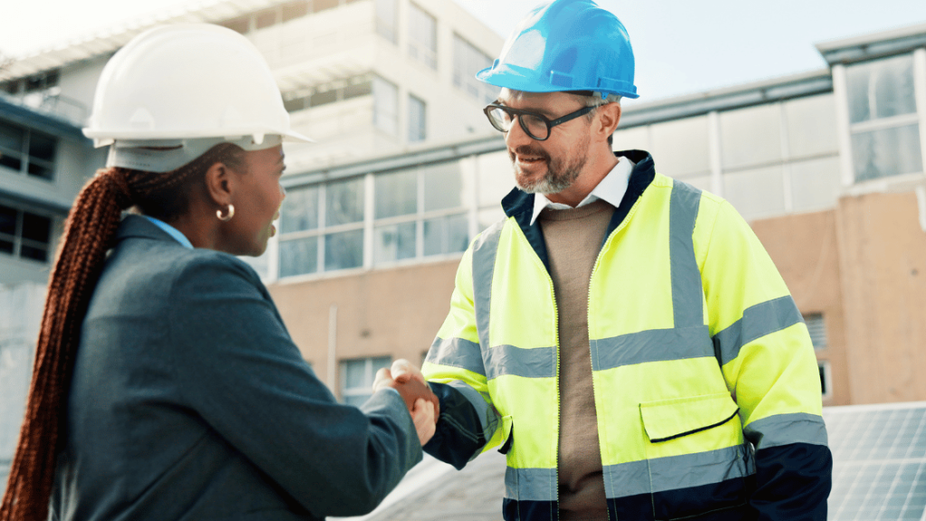 A man and a woman both wearing hard hats shaking hands